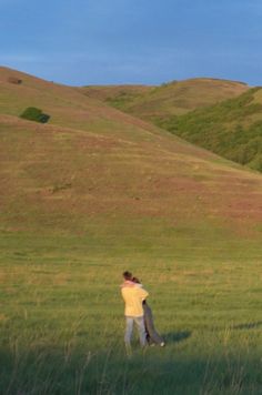 two people standing in a field with a kite flying over their heads and one holding the other's back