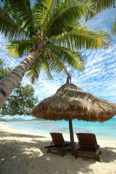 two lounge chairs under an umbrella on the beach