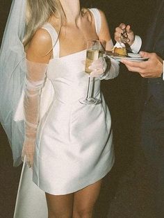 a woman in a white dress holding a plate with food on it while standing next to a man wearing a tuxedo