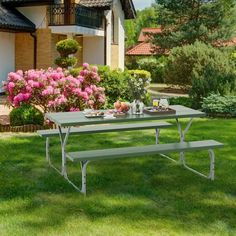 a picnic table in the middle of a lawn with pink flowers and bushes behind it