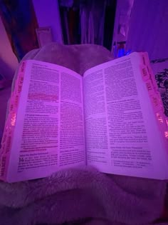 an open book sitting on top of a bed next to a purple light in a room