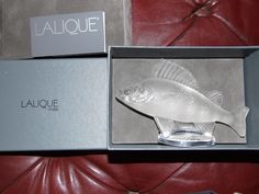 a glass fish in a box sitting on a leather couch next to a sign that says laque