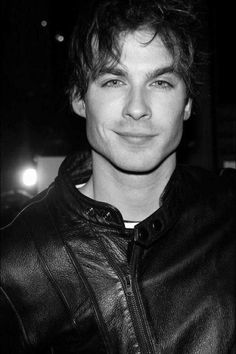 a black and white photo of a man in a leather jacket smiling at the camera