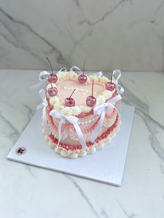 a three layer cake with cherries on top sitting on a white tablecloth next to a marble countertop