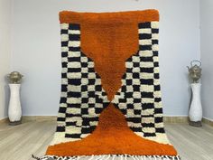 an orange, black and white rug is on the floor next to two vases