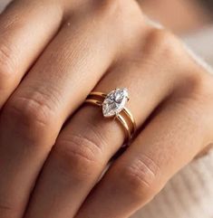 a woman's hand wearing a gold ring with a white diamond on the middle