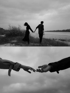 two people holding hands in front of a body of water and one person reaching out to the sky