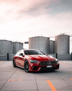 a red mercedes benz coupe parked in front of some silo silos and water tanks