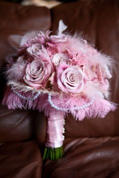 a bridal bouquet with pink roses and feathers on a brown leather couch in a living room