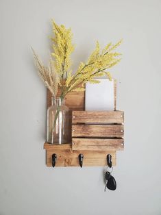 a vase with flowers and keys on a wooden shelf next to a key holder that is attached to the wall