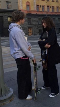 two people standing next to each other with skateboards in their hands on the sidewalk