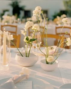 two white vases filled with flowers sitting on top of a table next to candles