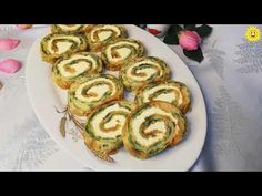 a white plate topped with spinach rolls on top of a table next to flowers