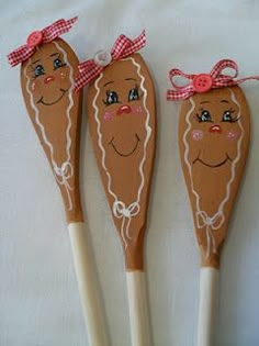 three wooden utensils with faces on them, one has a red bow and the other is brown