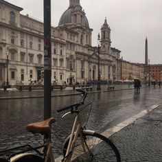 a bike parked on the side of a wet street next to tall buildings with towers