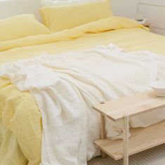 a bed with yellow linens and a white bowl on the end table next to it