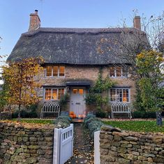 an old stone house with a thatched roof and white gate leading to the front door