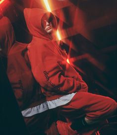 a man in a red hoodie is sitting on a chair with lights behind him