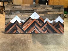 a wooden sign with mountains painted on it in the shape of chevron wood planks