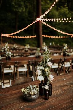 two vases filled with flowers sitting on top of a wooden table covered in lights