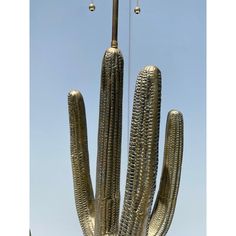 a large metal cactus sculpture in front of a blue sky with two lights on it