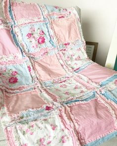 a pink and blue quilted blanket on a couch next to a pillow with flowers