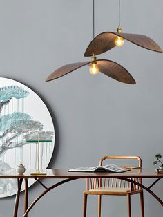 a dining room table with chairs and two pendant lights hanging over it, in front of a circular painting on the wall