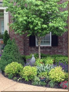 a brick house with trees and flowers in the front yard