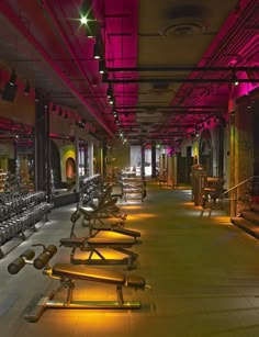 an empty gym with rows of treadmills lit up by neon lights in the ceiling