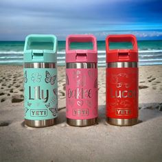 three insulated water bottles sitting on the beach