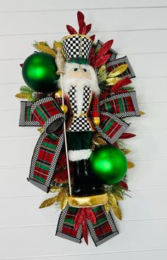 a christmas wreath with a santa clause holding two green baubles and an ornament