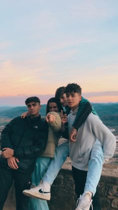 four young men posing for a photo on top of a mountain at sunset with the sun setting in the background