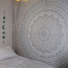 a bed with a white comforter next to a large wall hanging on the wall