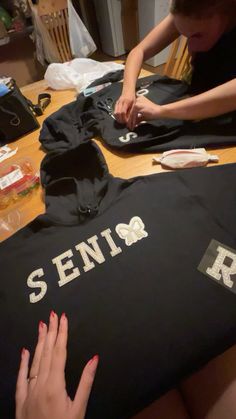 a woman sitting at a table working on some t - shirts that are being sewn