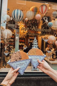 two people holding up some kind of item in front of a store window with hot air balloons