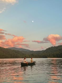 two people in a small boat on a lake with mountains in the background at sunset