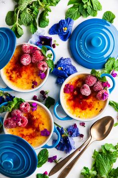 three bowls filled with pudding and raspberries on top of blue plates next to flowers