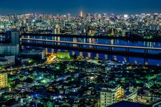 an aerial view of a city at night with lights on and bridges in the distance