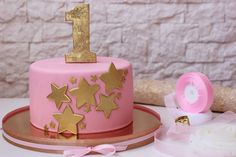 a pink birthday cake with gold stars on it and a candle next to the cake