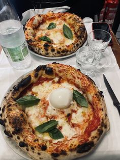 two pizzas sitting on top of a white table