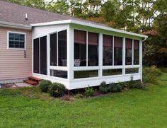 a screened in porch on the side of a house with grass and trees around it