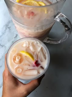 a person holding a drink in front of a pitcher filled with ice and lemon wedges