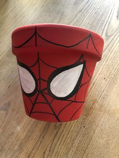 a red cup with a spiderman face painted on it's side sitting on top of a wooden table