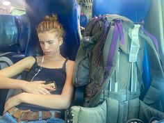 a woman sitting in an airplane looking at her cell phone while listening to headphones