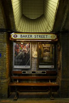 an underground train station with a bench and sign for baker street on the wall above it