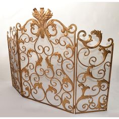 an ornate gold metal fireplace screen with scrolls and leaves on the sides, set against a white background