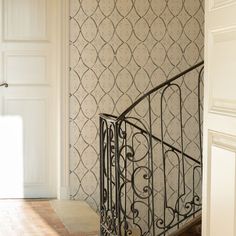 an iron stair railing in front of a wallpapered room with white walls and doors