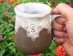 a hand holding a coffee cup with lace on it and flowers in the back ground