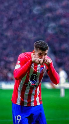 a soccer player in red and white is on the field with his hand to his face