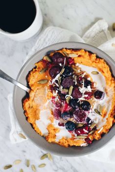 a bowl filled with fruit and yogurt on top of a white table next to a cup of coffee